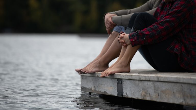 water, the edge of a dock and the lower halves of two people with rolled up pant legs