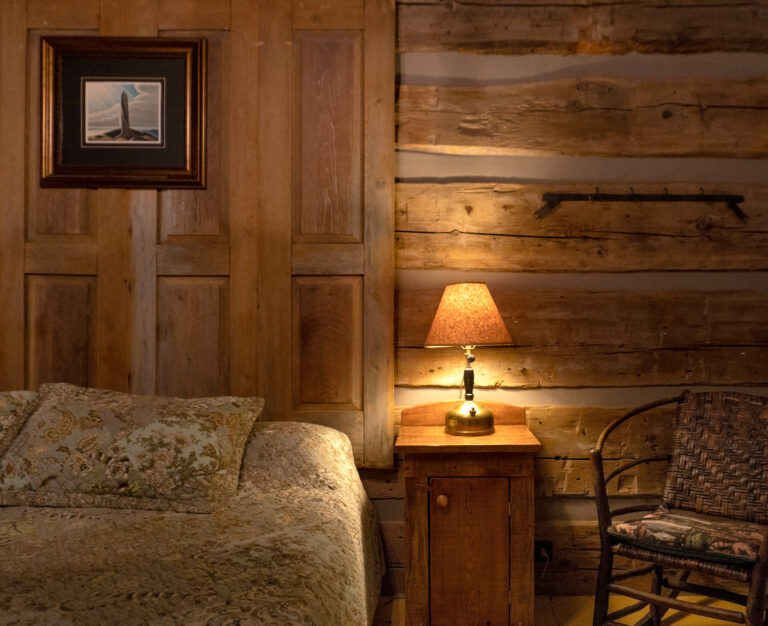 interior of a log cabin with bed, wooden nightstand, vintage wood rocking chair and iluminated brass table lamp
