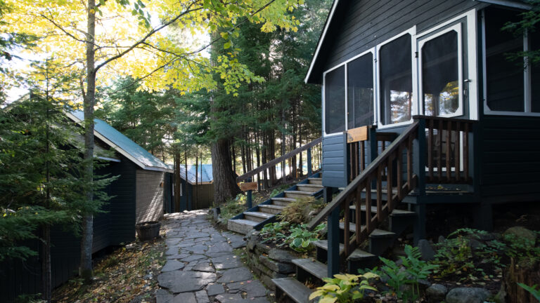 flagstone path leading through the woods with a dark brown cabin on the right and two other cabins further along the path