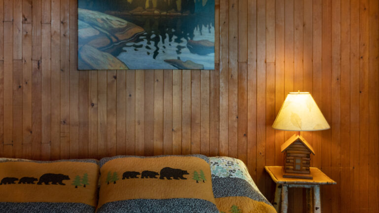 wood-paneled wall with lit bedside table lamp, group of seven artwork and bear-themed pillows