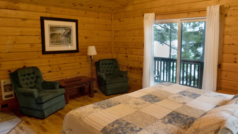 two green upholstered chairs and the end of a bed with a blue and white patch work quilt inside a log cabin