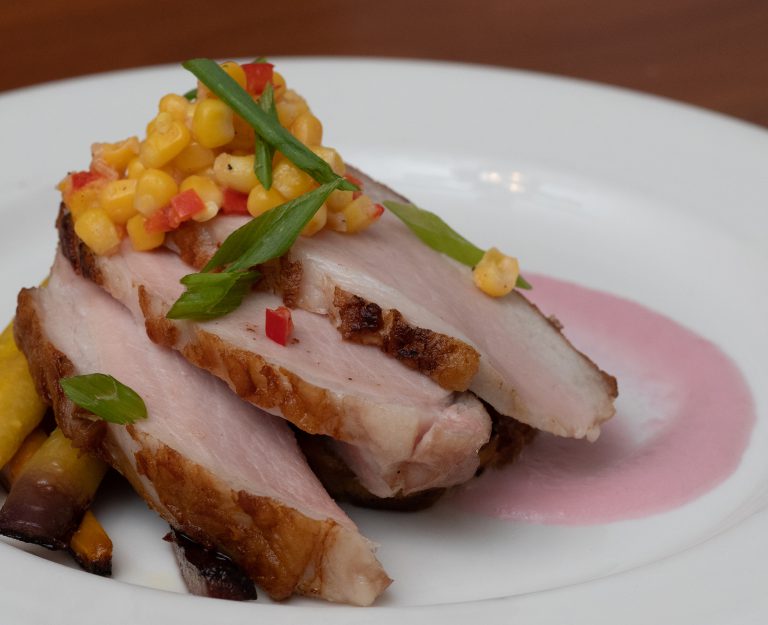 close up of sliced pork loin road topped with corn salsa on a white dinner plate