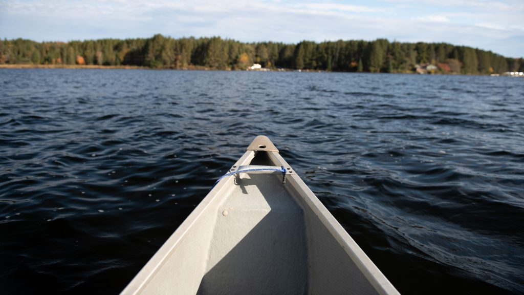 view from inside a canoe of Chache Lake, the shoreline and the front end of a canoe