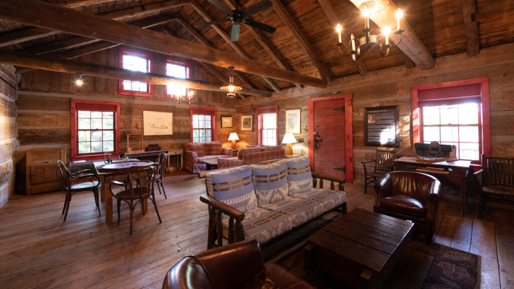 Interior of large log cabin with two seating areas and an antique wood dining table and chairs
